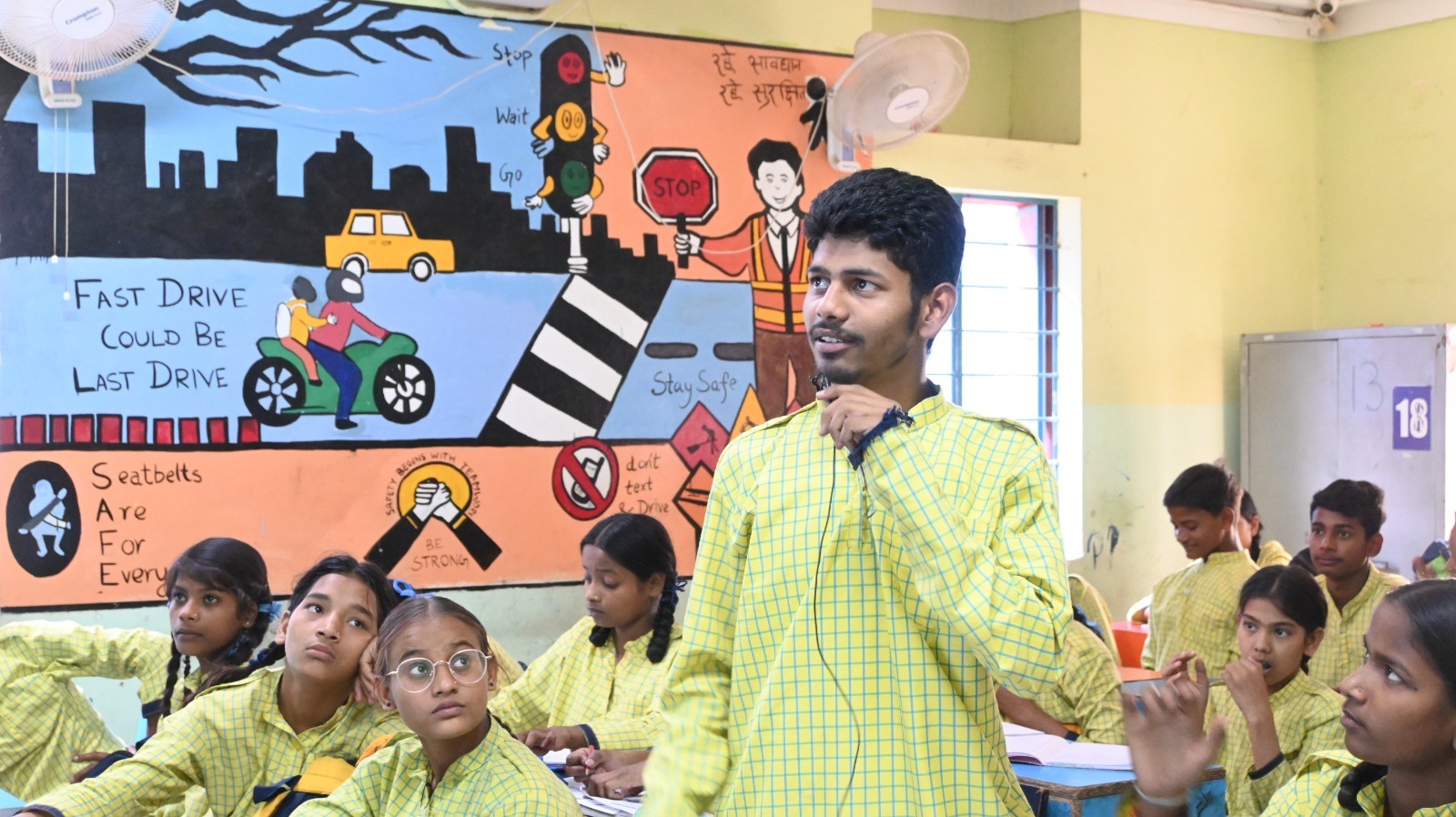 A presenter speaking at the front of the class with safety murals in the background