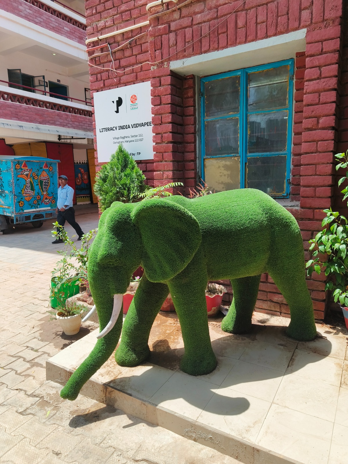 Entrance to Literacy India Vidyapeeth — a green topiary elephant in front of the school sign