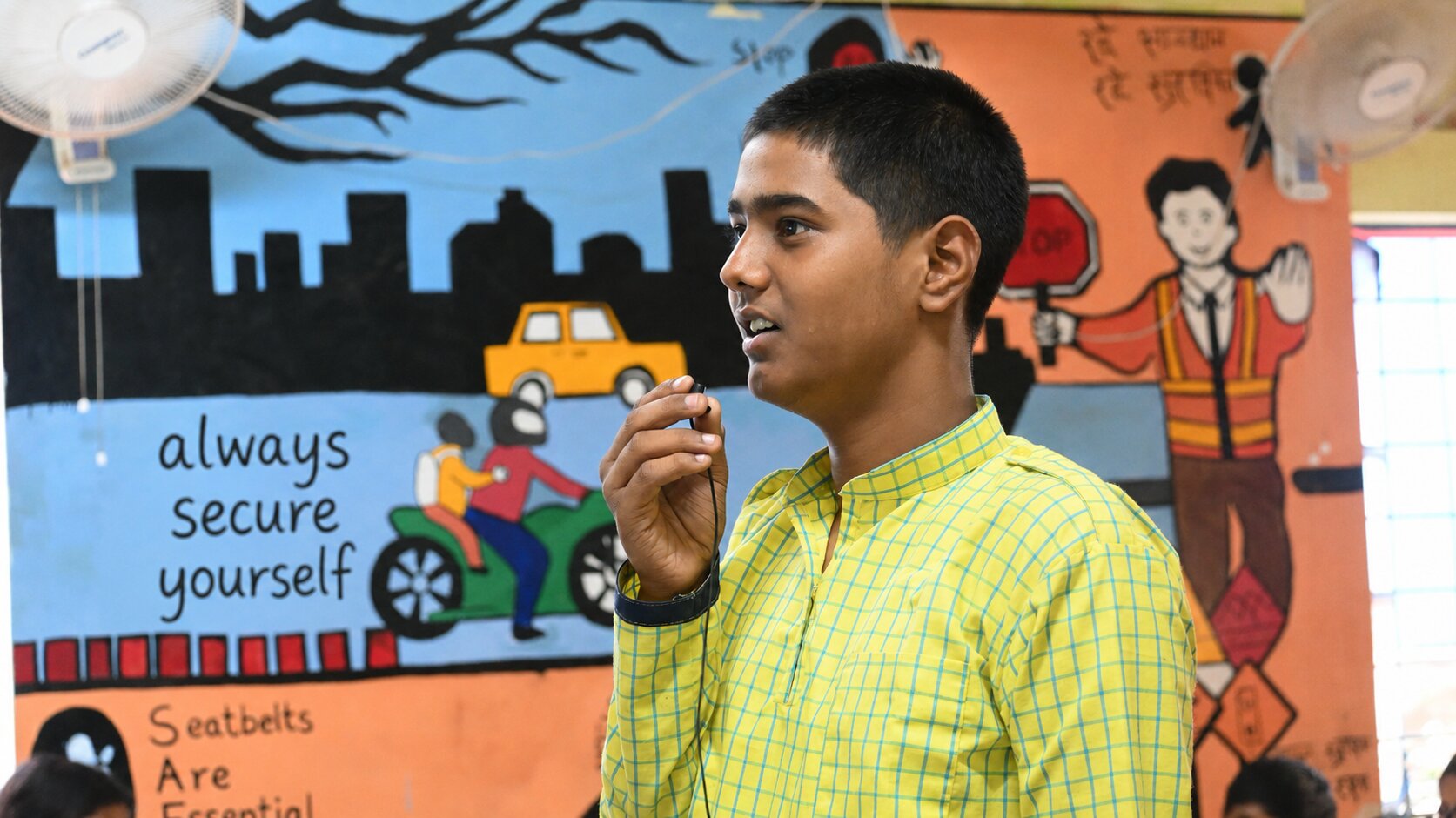 A student speaking during a FinLight workshop, with the words 'always secure yourself' painted on the classroom mural behind him